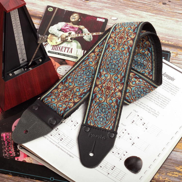 wide long jacquard guitar strap with floral pattern placed next to metronome and sheet music