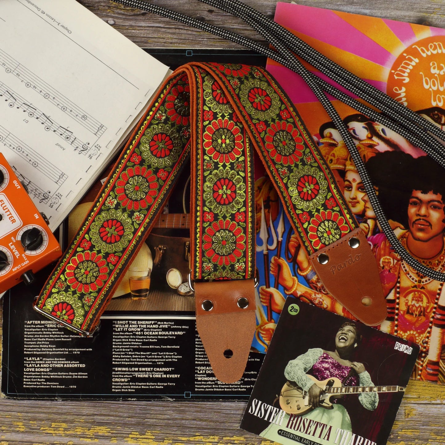 Amber Parade woven guitar strap displayed among vinyl records and a guitar pedal, highlighting its warm decorative pattern and detailed textile construction.