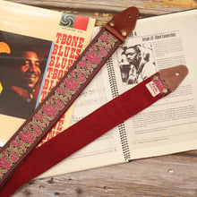 Azalea floral guitar strap displayed with sheet music and a T-Bone Walker vinyl, showing its pink and gold jacquard pattern, Burgundy Red suede backing, dark brown leather ends and antique gold hardware.