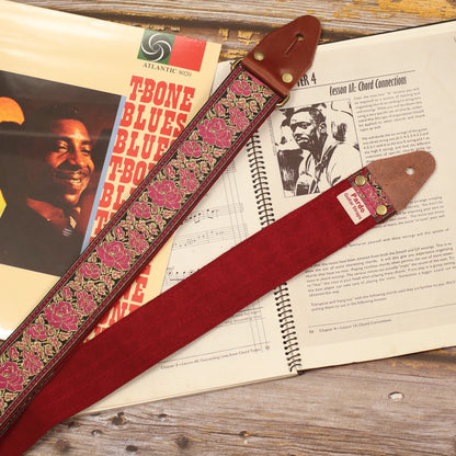 Azalea floral guitar strap displayed with sheet music and a T-Bone Walker vinyl, showing its pink and gold jacquard pattern, Burgundy Red suede backing, dark brown leather ends and antique gold hardware.