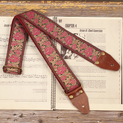 Azalea retro floral jacquard guitar strap displayed on a sheet music book, showcasing the complete pink and gold woven floral pattern and handcrafted design.