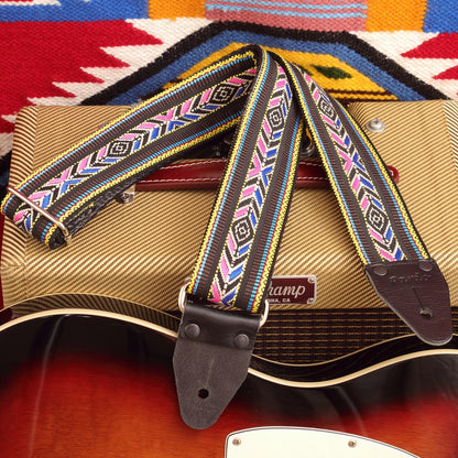 The Black Cherokee Indigenous Style Guitar Strap displayed alongside a guitar amplifier, creating a complete stage-ready setup for musicians.