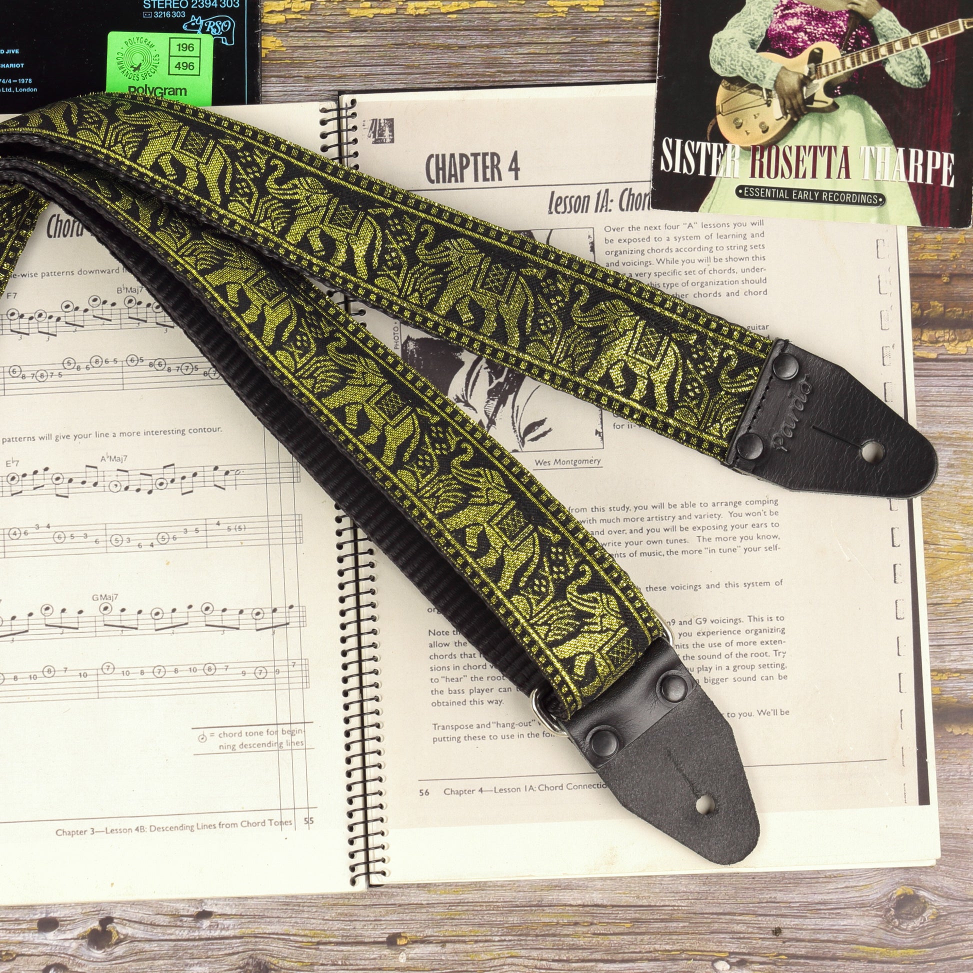 Black and gold elephant jacquard guitar strap displayed across an open sheet music book