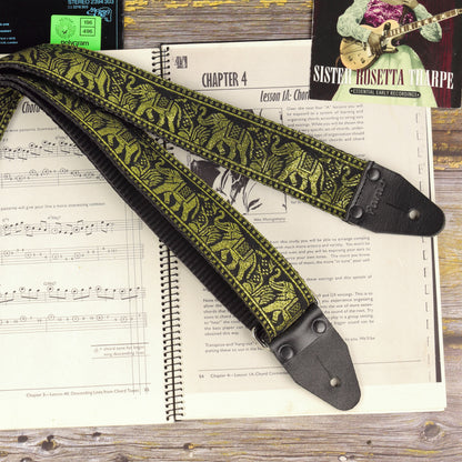 Black and gold elephant jacquard guitar strap displayed across an open sheet music book
