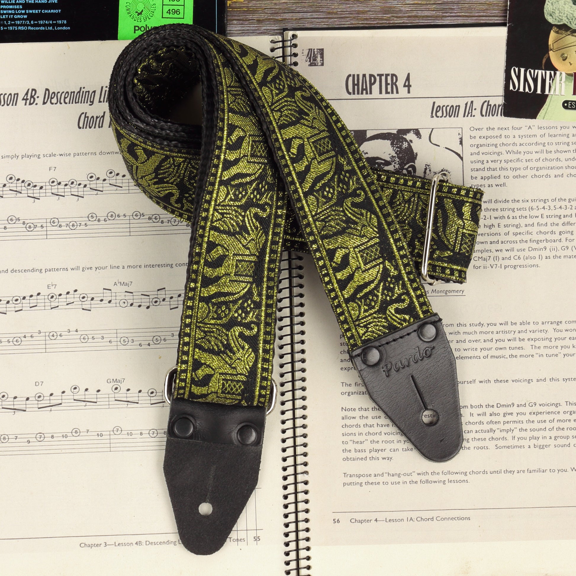 Close-up of the Black and Gold elephant jacquard guitar strap with black leather ends on a sheet music book