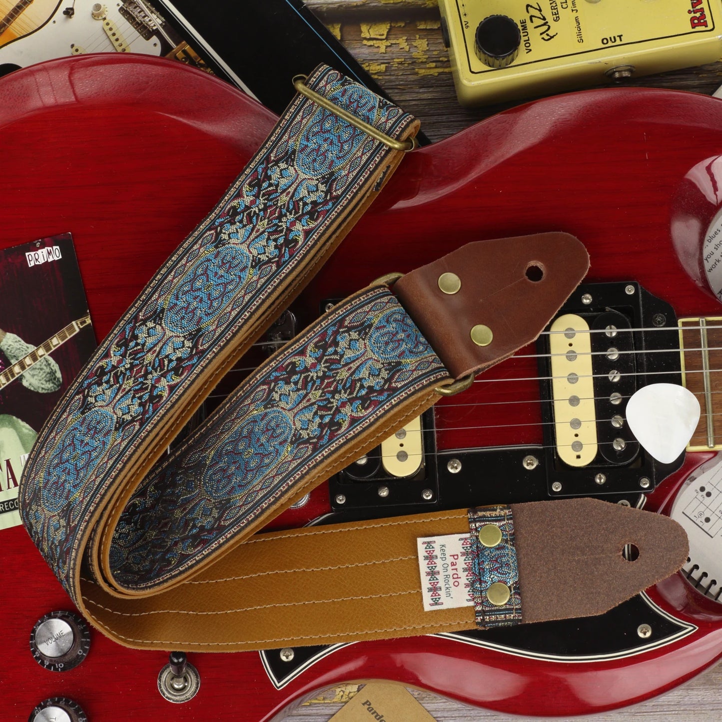 Blue Garden guitar strap displayed on a cherry red Gibson SG, with Clear Vinyl backing, dark brown leather ends and Antique Gold hardware.