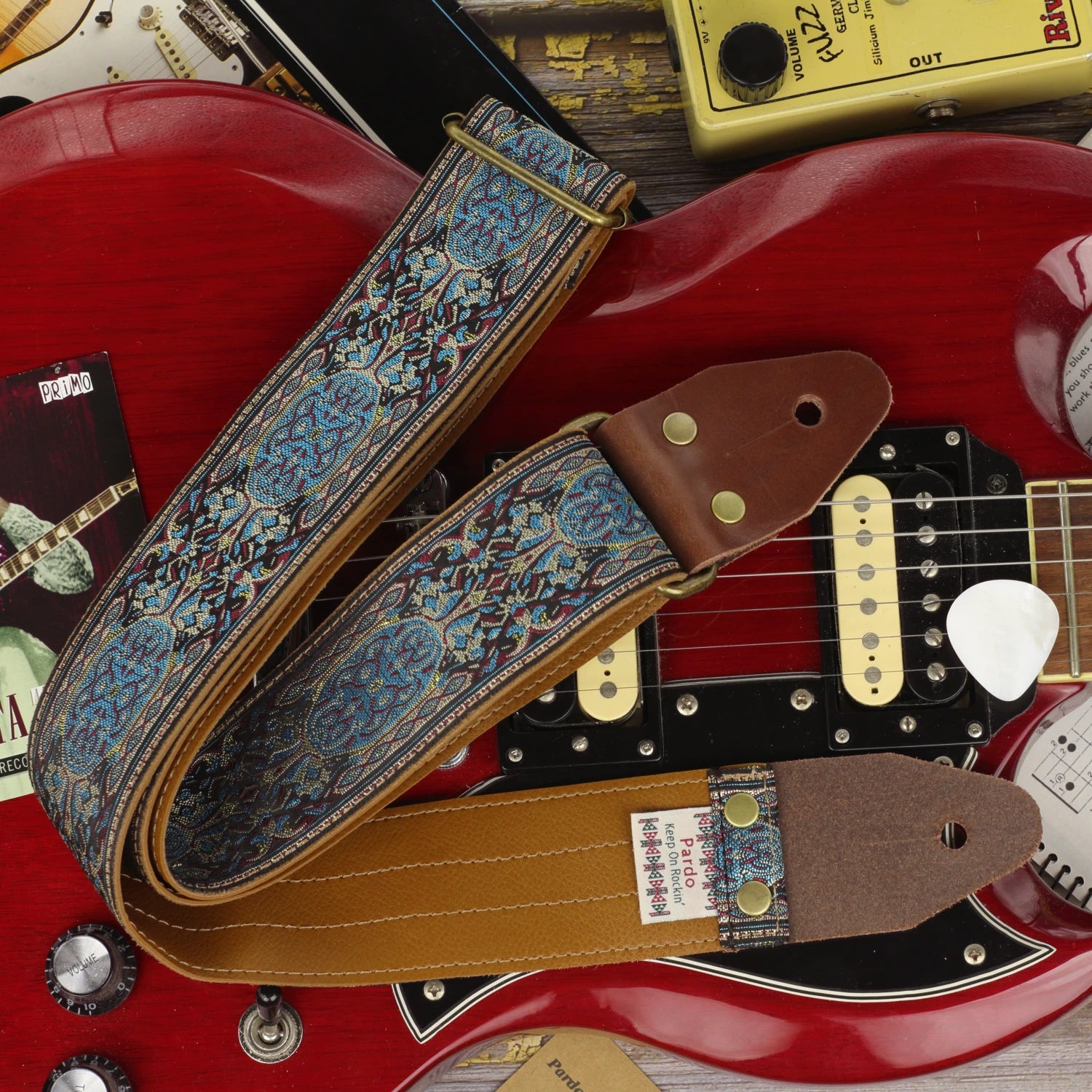 Blue Garden guitar strap displayed on a cherry red Gibson SG, with Clear Vinyl backing, dark brown leather ends and Antique Gold hardware.