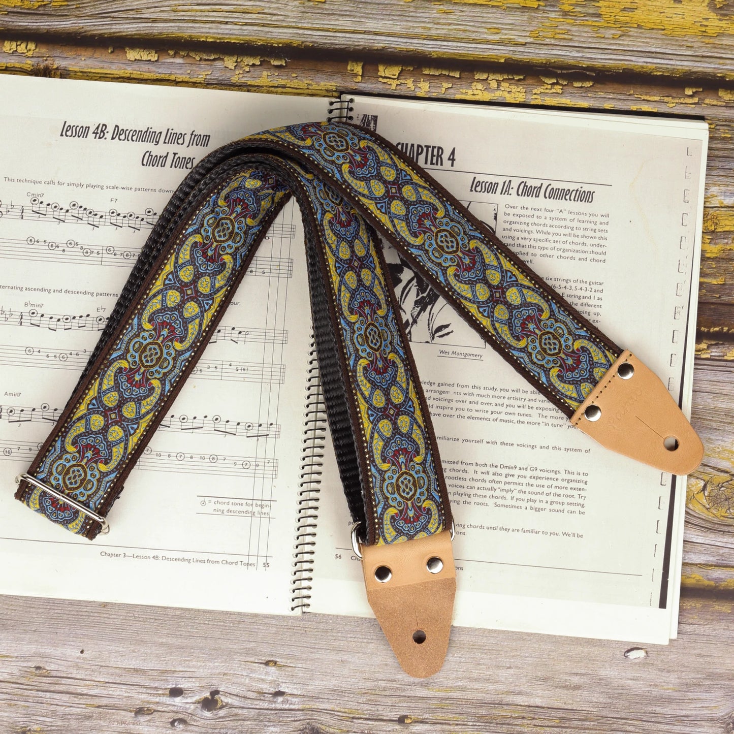 Blue lake guitar strap displayed on a sheet music book, showing its intricate turquoise, ivory and pink woven pattern.
