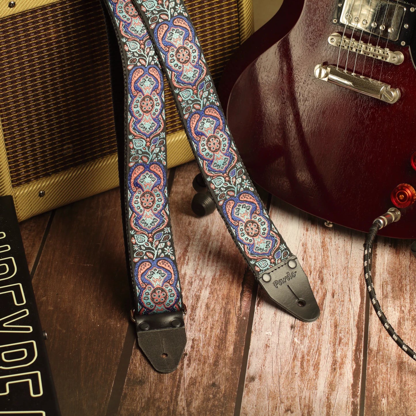 Blue Mirage handmade guitar strap displayed with a Gibson SG and Fender Champ amplifier in a studio setting