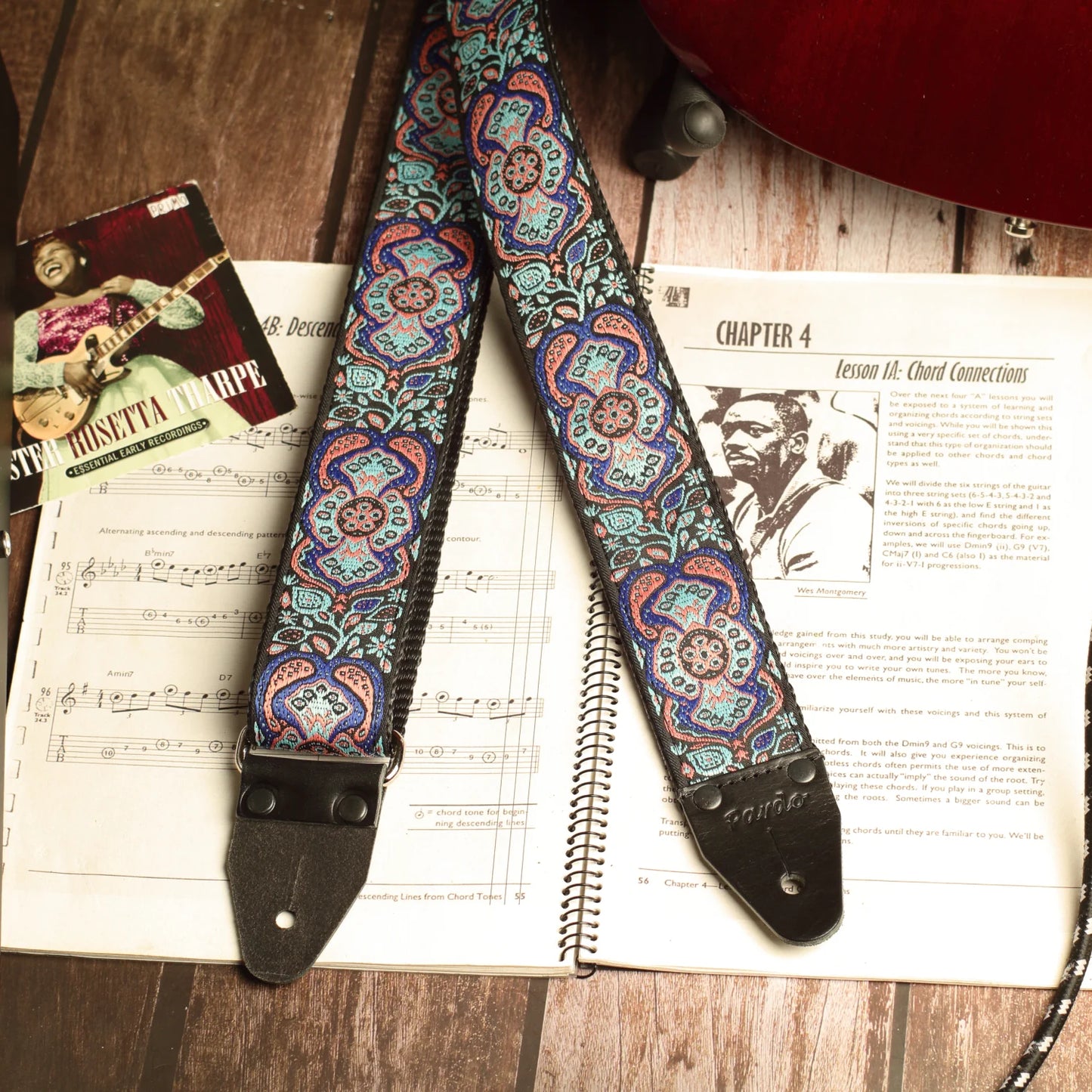 Blue Mirage handmade guitar strap showing jacquard fabric and genuine leather ends resting on a vintage guitar sheet music book