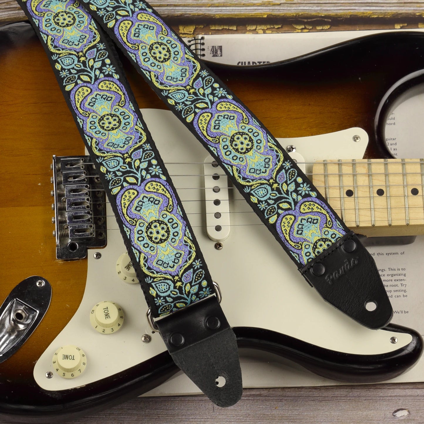 Close-up of the Blue Paisley guitar strap on a Fender Stratocaster, showing its jacquard pattern and black leather ends.