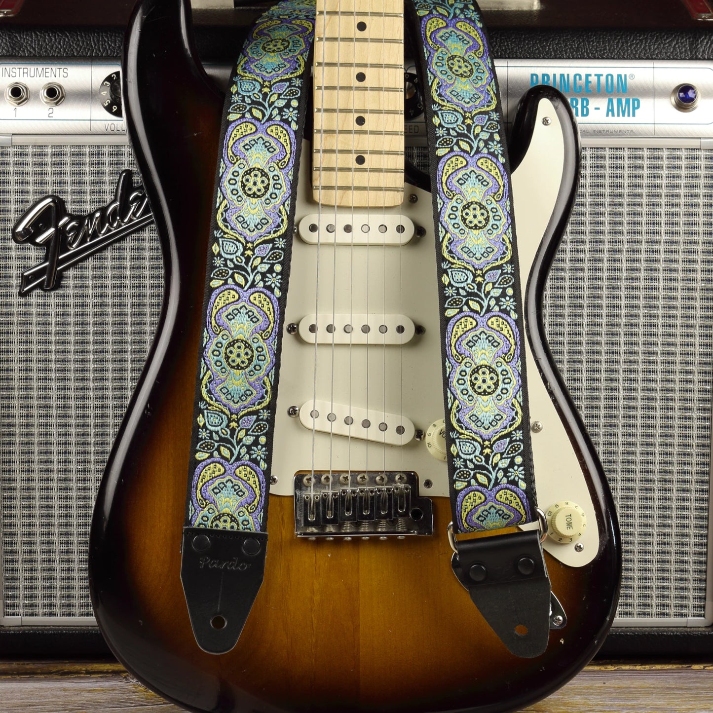 Blue Paisley guitar strap displayed with a sunburst Fender Stratocaster and a Fender Princeton Reverb amplifier.