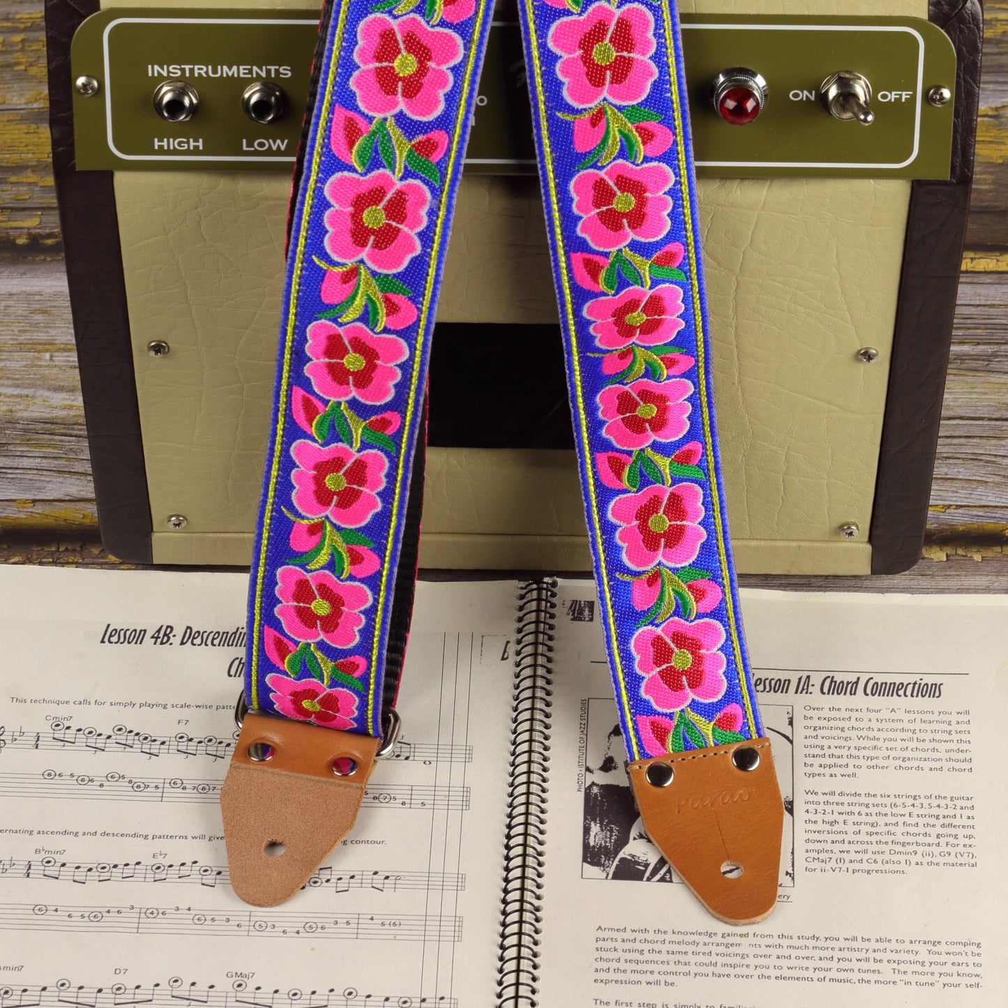 Blue Serenade guitar strap displayed with a Fender Champion 600 amplifier and a sheet music book.