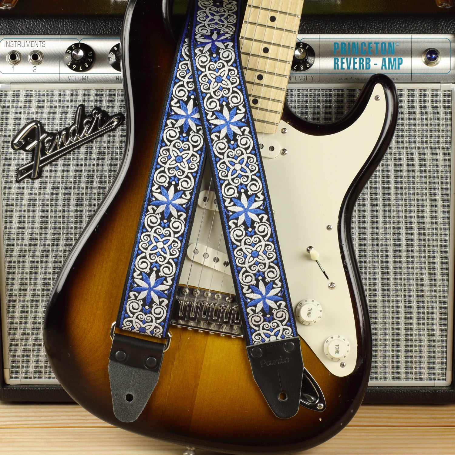 Featuring a Fender Stratocaster in sunburst with a Fender Princeton Reverb, this blue and white mosaic guitar strap showcases an intricate geometric pattern with continuous visual flow.