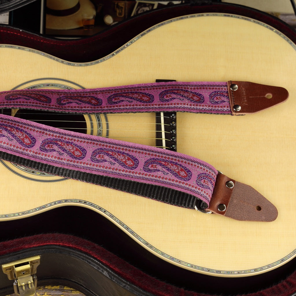 Bohemian-style guitar strap with a soft lilac paisley pattern, shown on a parlor acoustic guitar. Handmade, adjustable, and designed for comfort and vintage-inspired flair.