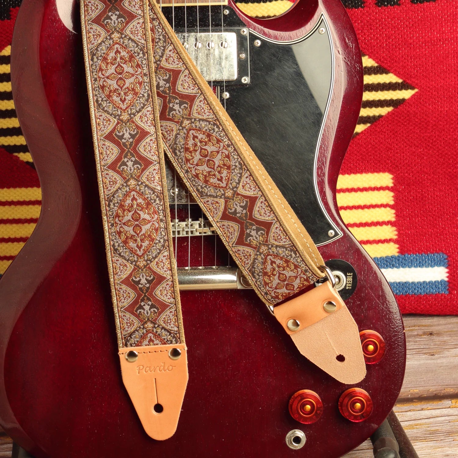 Brown Mountain handmade jacquard guitar strap with vintage brown psychedelic pattern displayed on a cherry red SG-style electric guitar with natural leather ends.
