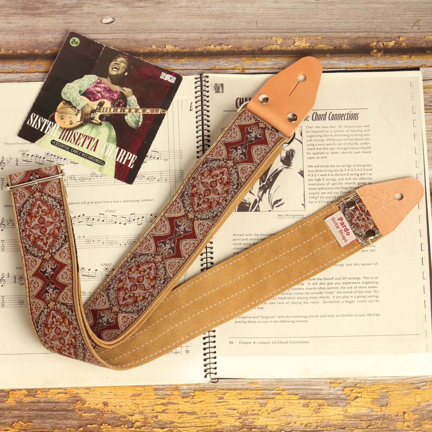 Brown Mountain psychedelic jacquard guitar strap with earth-tone vintage pattern displayed on an open guitar chord book beside a Sister Rosetta Tharpe album cover. Handmade artisan guitar strap with suede backing.