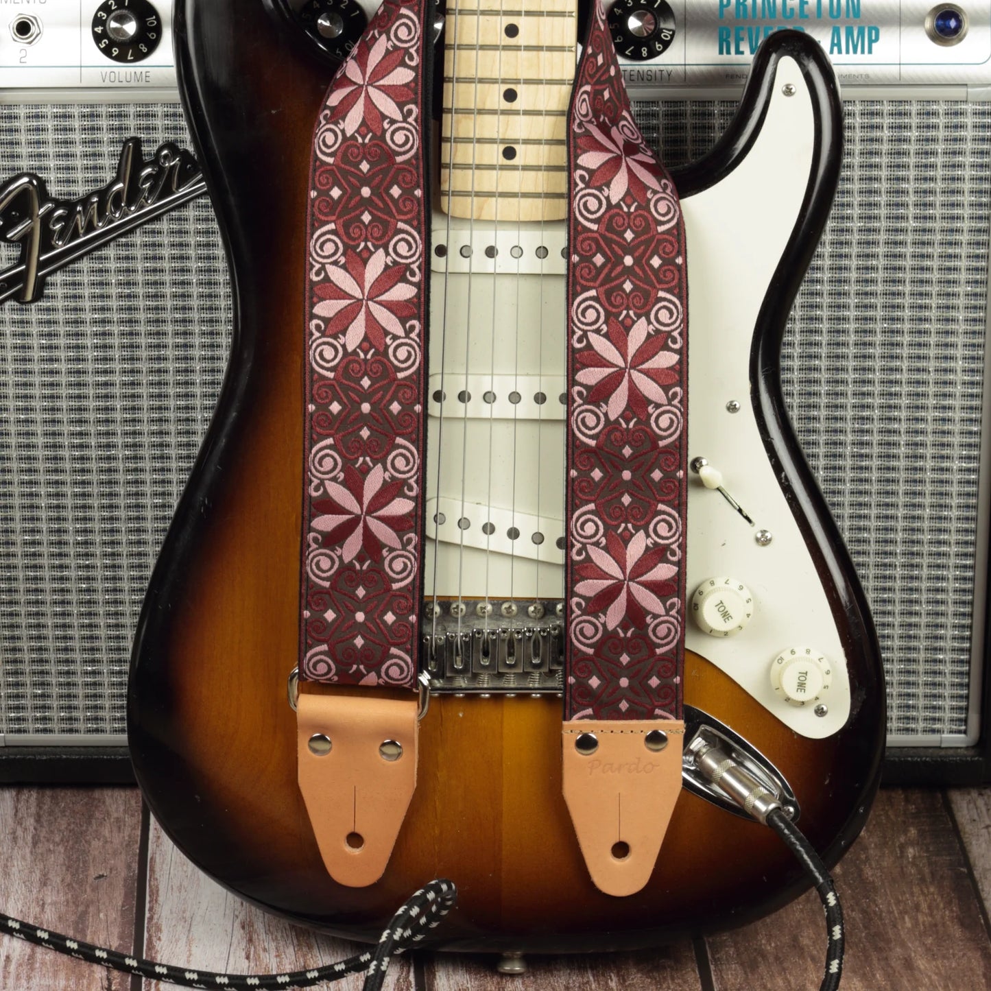 Burgundy red mosaic guitar strap shown with a Fender electric guitar and a Fender Princeton Reverb, emphasizing a dense geometric pattern and deep visual texture.