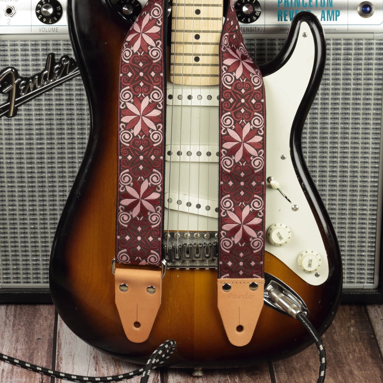 Burgundy red mosaic guitar strap shown with a Fender electric guitar and a Fender Princeton Reverb, emphasizing a dense geometric pattern and deep visual texture.