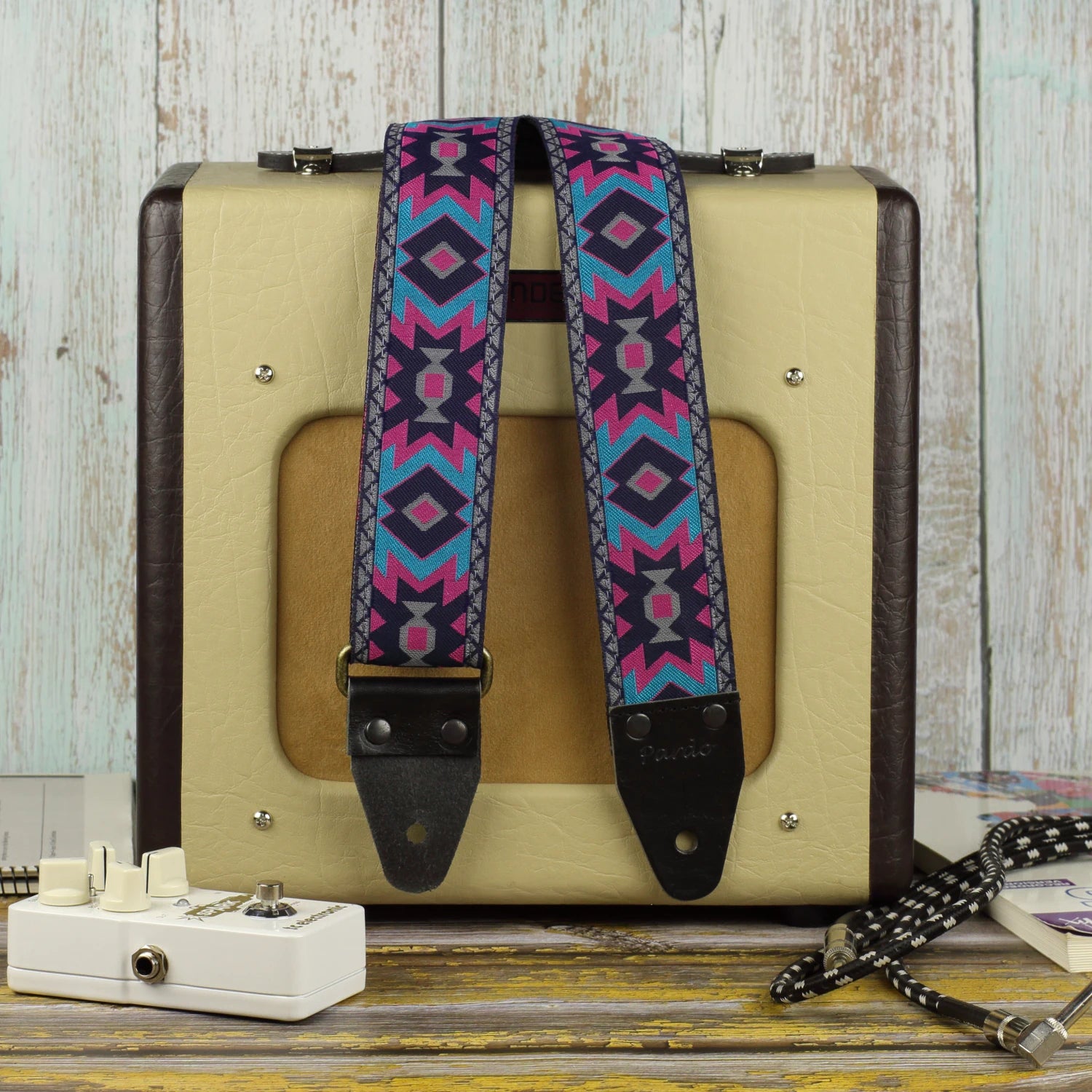 Canyon Pulse guitar strap displayed beside a Fender Champion 600 amplifier, showing its turquoise, magenta, gray and black geometric design.