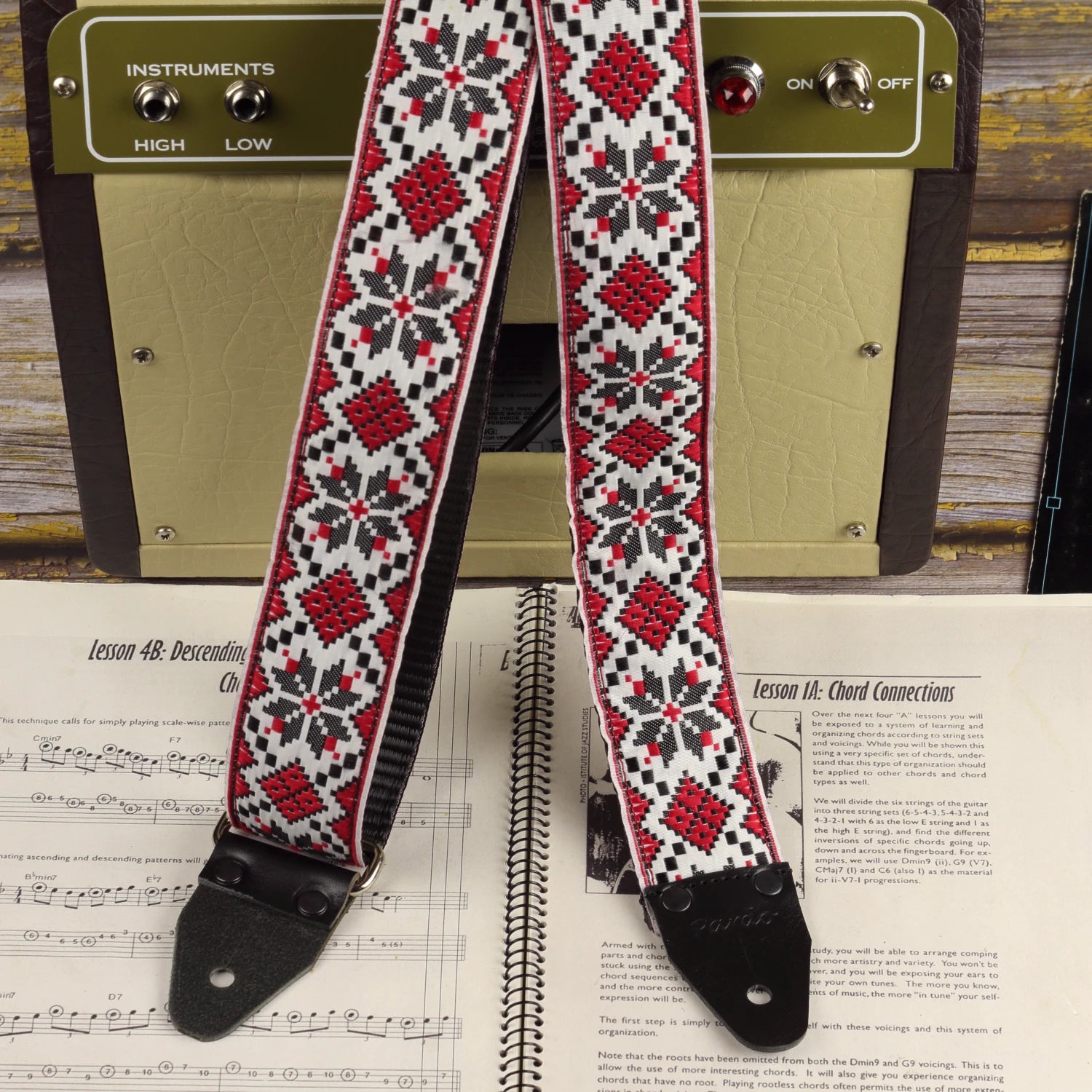 Crimson Compass guitar strap displayed beside a Fender Champion 600 amplifier, featuring its symmetrical red, black and ivory woven design.