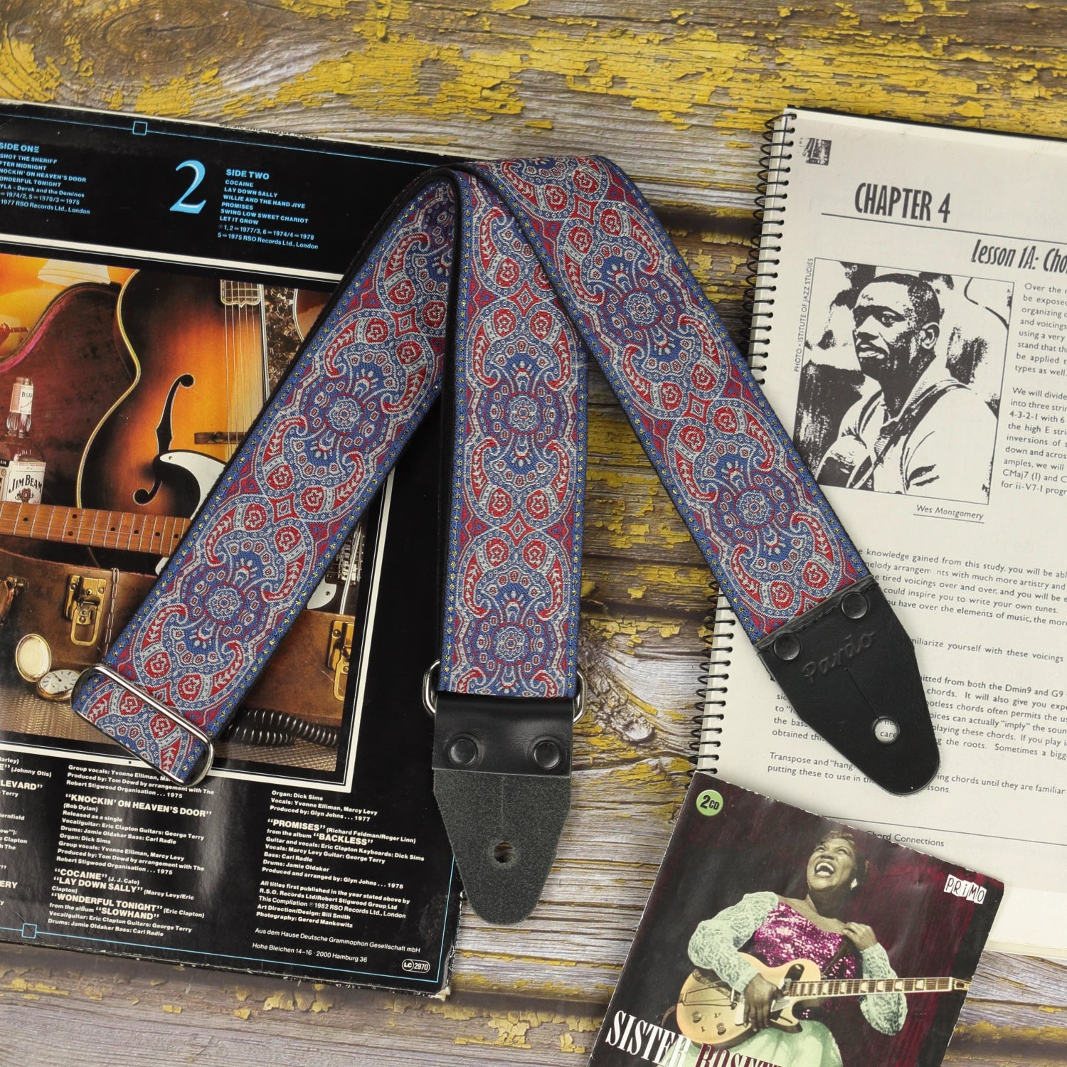 Close-up of the Efrit guitar strap with black leather ends, displayed with sheet music and vinyl records.