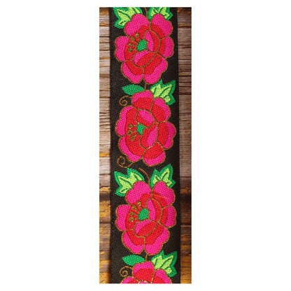 Close-up of the Midnight Cameo guitar strap design with layered pink and red motifs, green leaves and golden details on a black background.