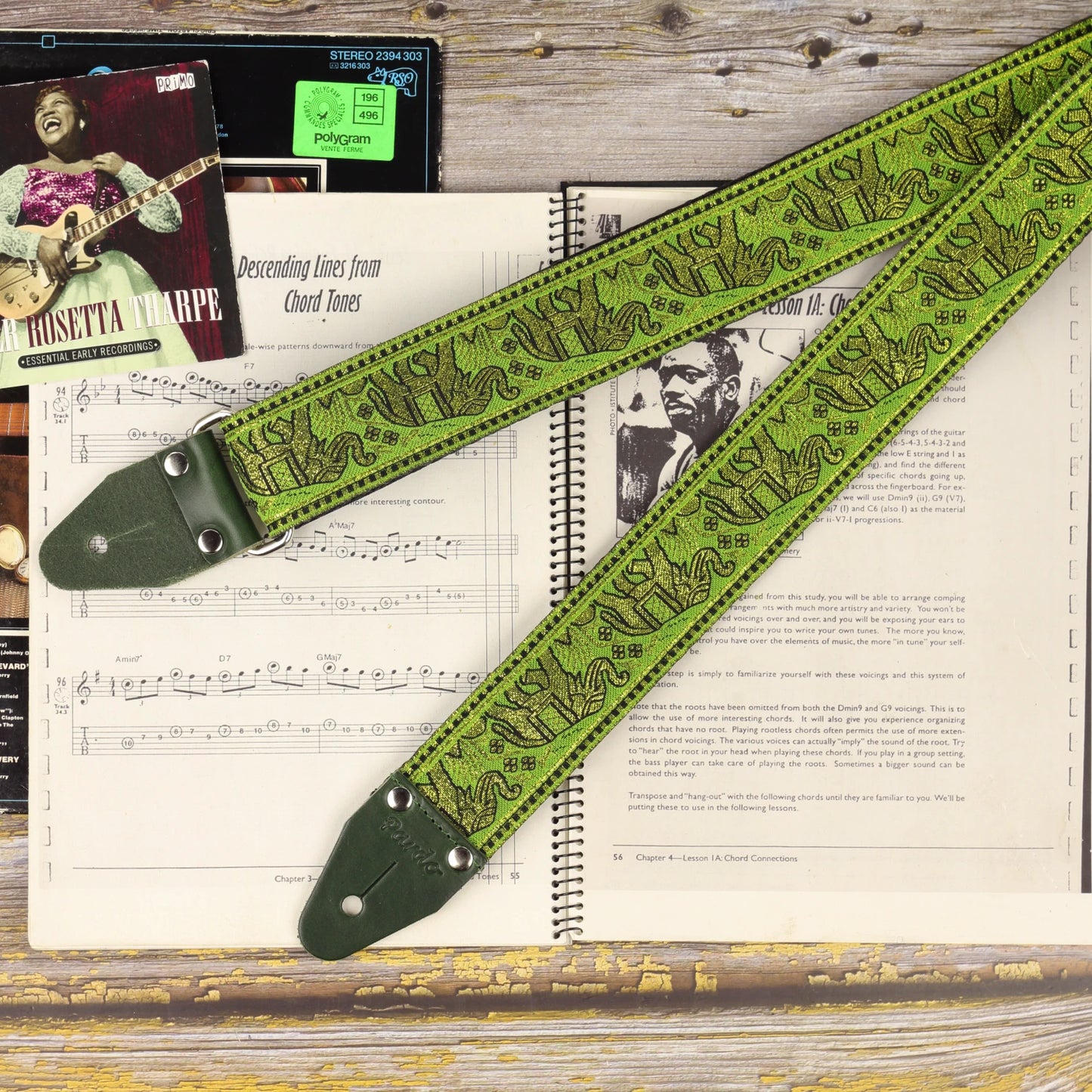 Green and gold elephant jacquard guitar strap with green leather ends displayed on an open sheet music book