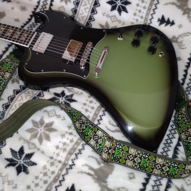 Green electric guitar paired with a Green Woodstock guitar strap featuring a colorful woven jacquard pattern.