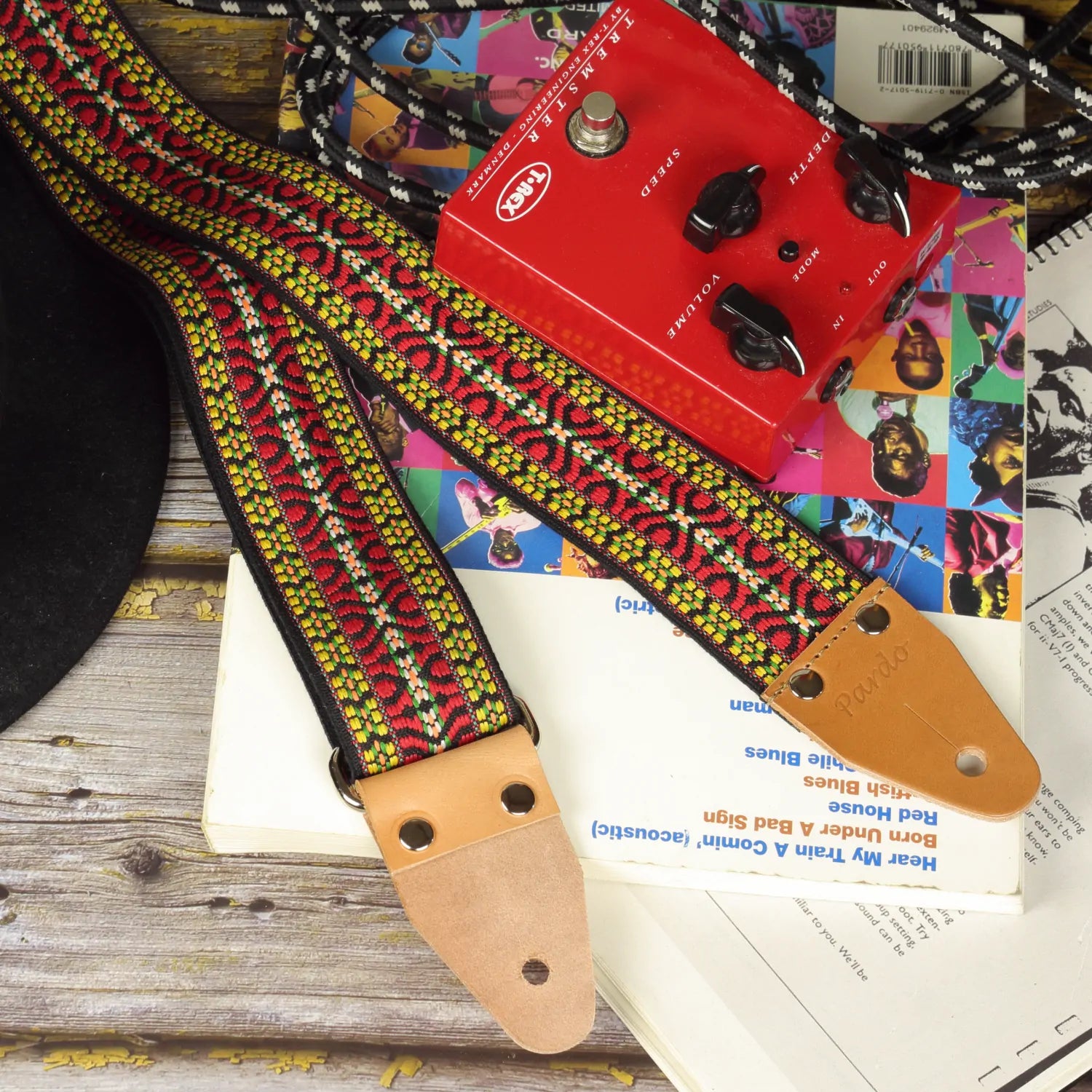 Artists hootennany guitar strap with psychedelic patterns, paired with songbook and guitar pedal
