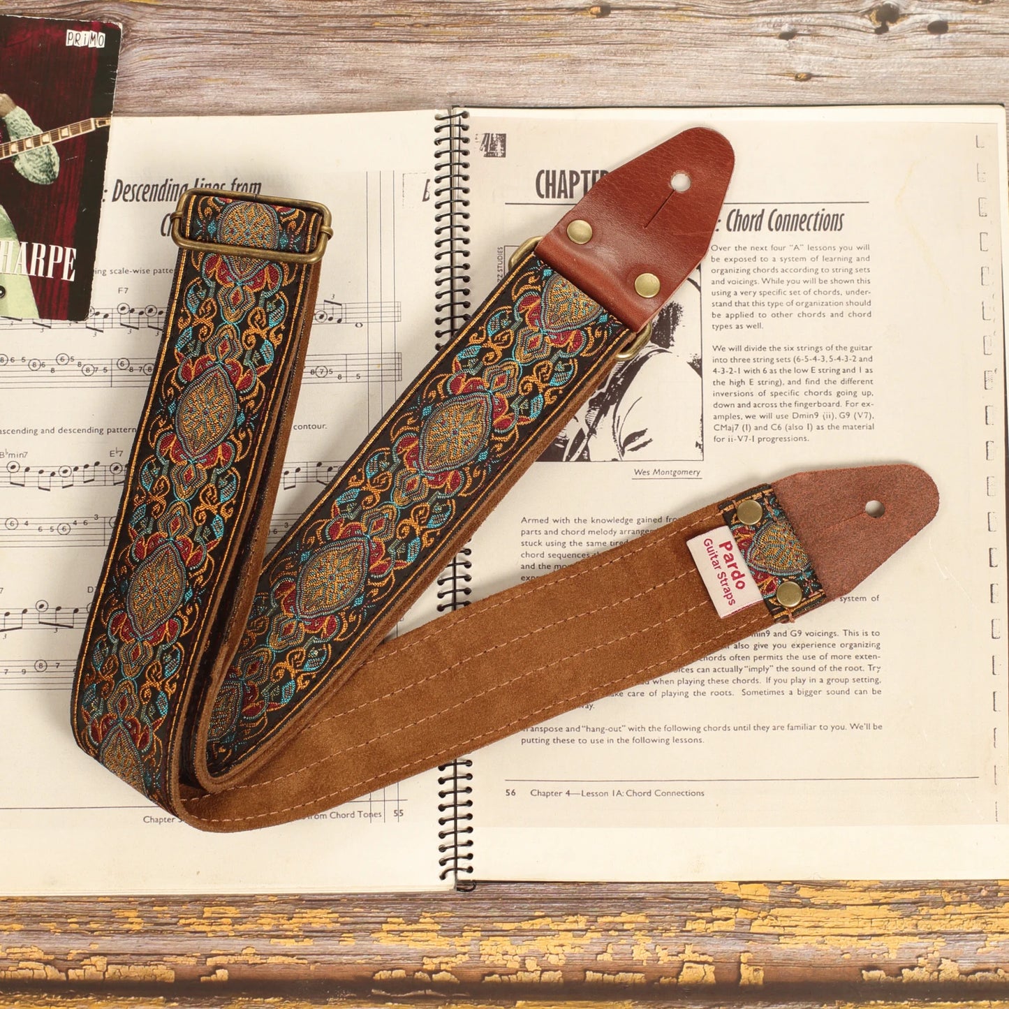 Loyalty multicolored jacquard guitar strap displayed on a sheet music book, showcasing the dark brown suede backing and handcrafted construction.