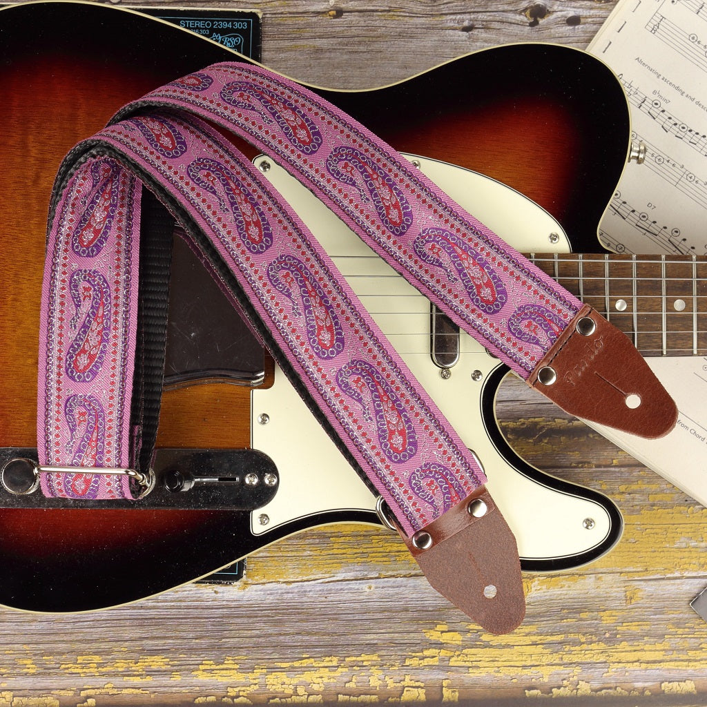 A handcrafted guitar strap with a lilac paisley pattern, made from woven jacquard fabric. Fits electric, acoustic, and bass guitars. Stylish, adjustable, and built for comfort with durable leather ends.