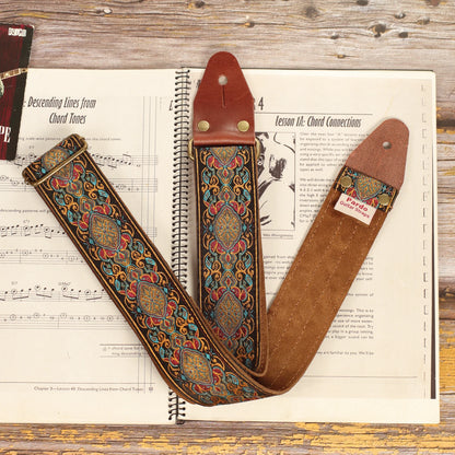 Close-up of the Loyalty multicolored jacquard guitar strap on a sheet music book, highlighting the woven fabric, dark brown suede backing, and handcrafted finish.