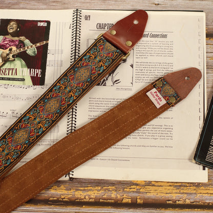 Detailed view of the Loyalty guitar strap showing the multicolored jacquard weave and dark brown suede backing on a sheet music book.