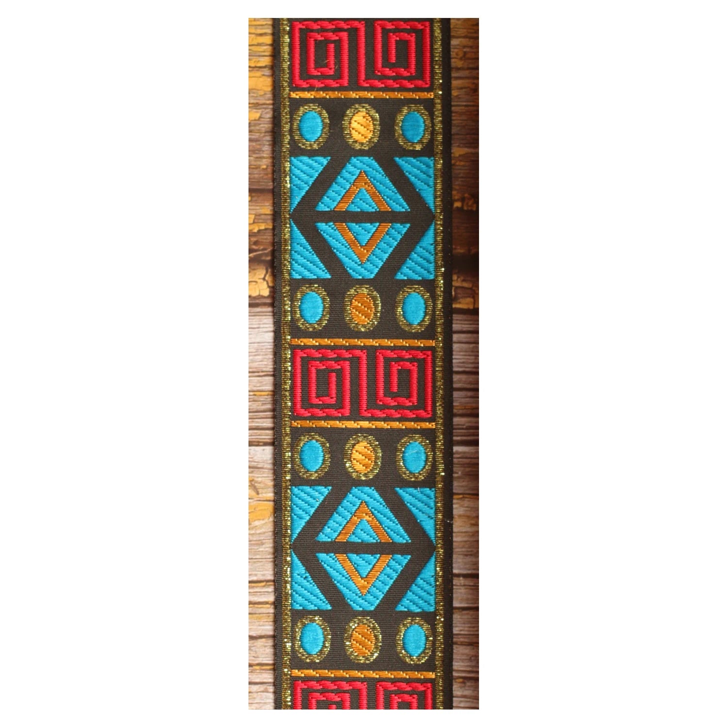Close-up of the Sunstone Circuit guitar strap design featuring turquoise, red and golden geometric panels on a dark background.