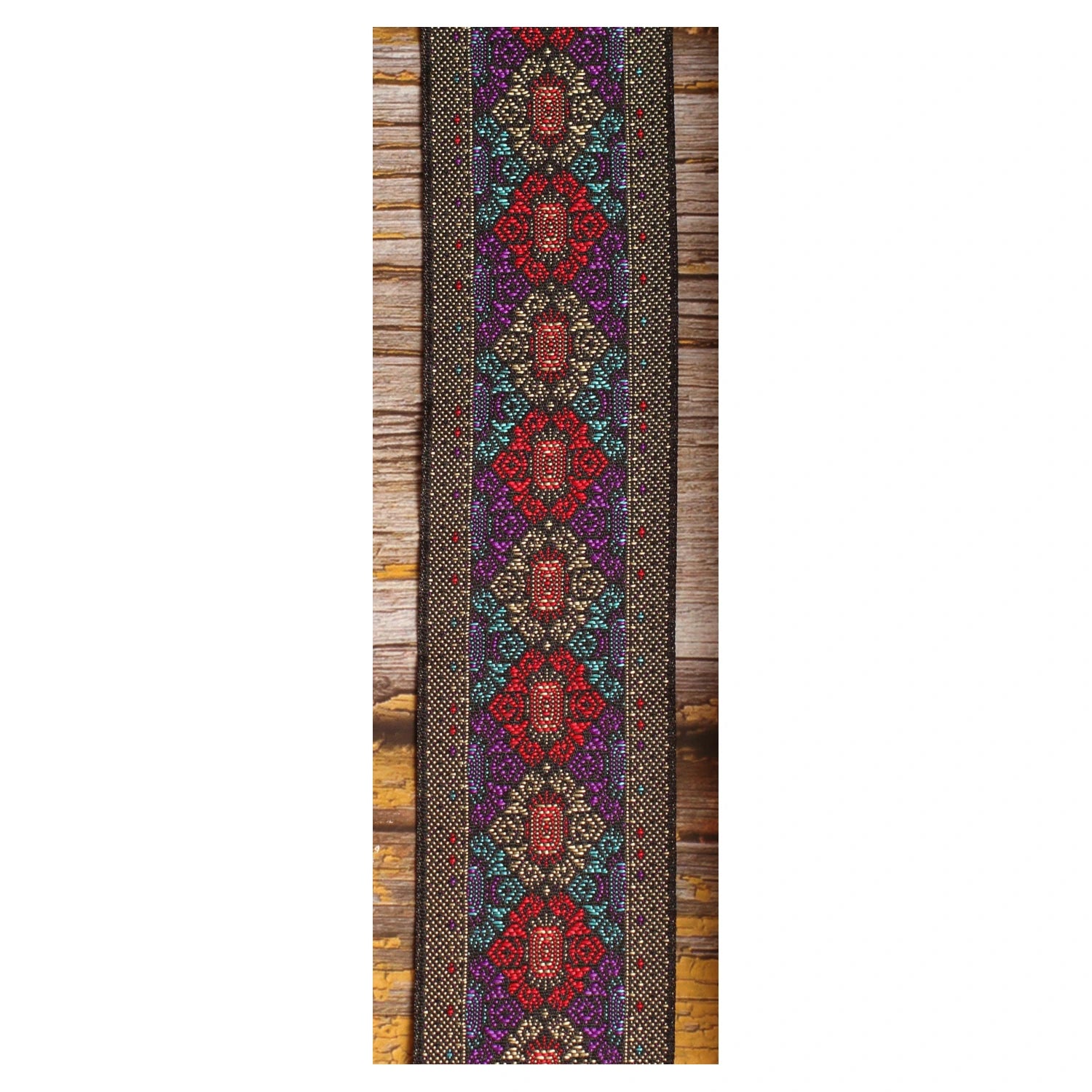 Close-up of the Purple Frame guitar strap design featuring intricate red, purple and turquoise motifs with metallic details on a dark background.