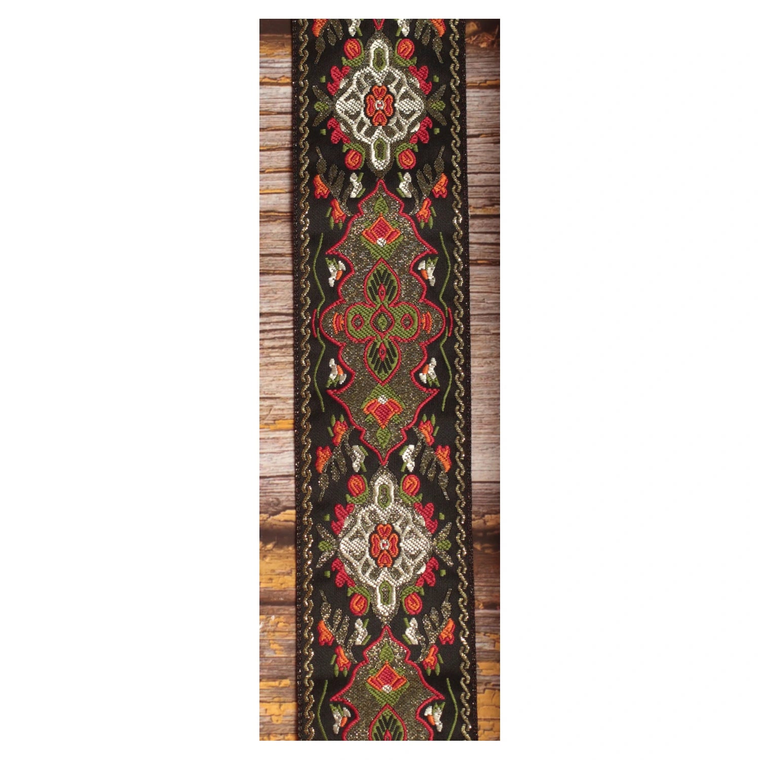 Close-up of the Red Fly guitar strap design with symmetrical red, olive green, ivory and orange details against a black background.