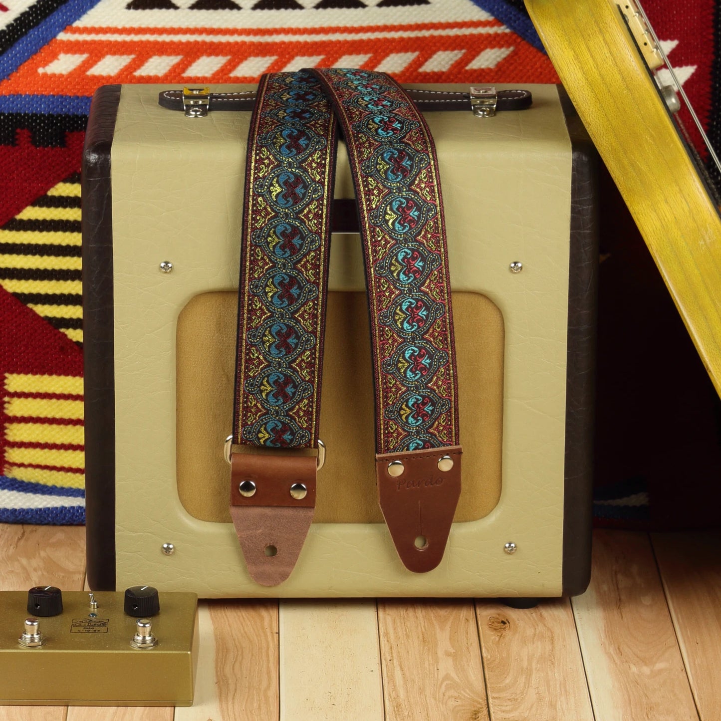 Pilgrim guitar strap displayed beside a Fender Champion 600 amplifier, showing its turquoise, red and golden woven design.