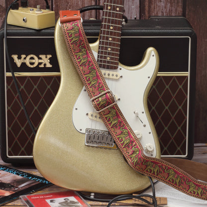 Pink and gold elephant jacquard guitar strap displayed with a Fender Stratocaster and Vox AC10 guitar amplifier