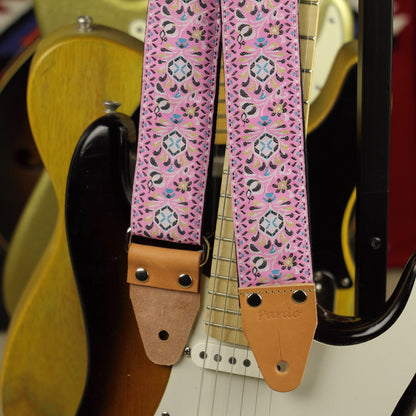 Pink Pheasant jacquard guitar strap with brown leather end and electric guitars in the background