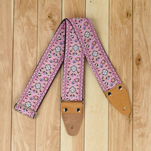 Pink Pheasant jacquard guitar strap arranged in a triangle on a wooden background