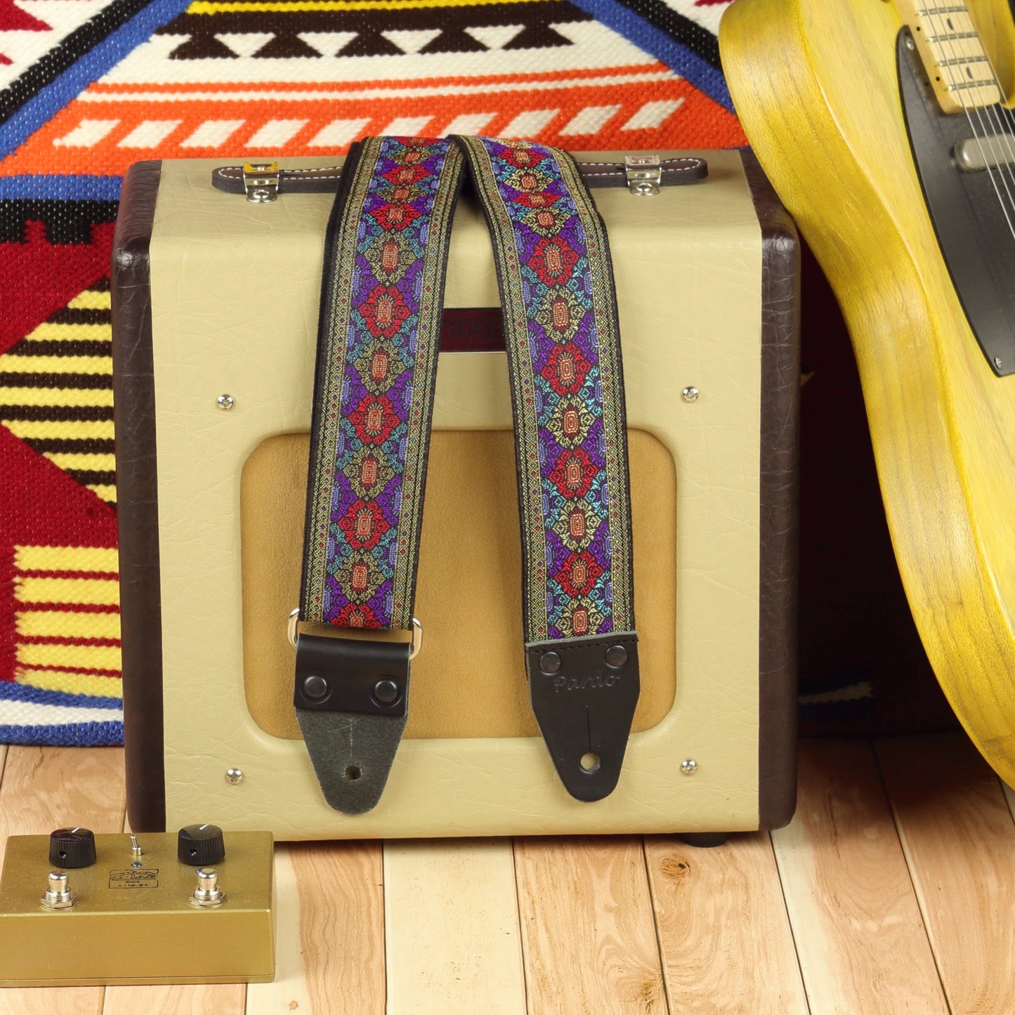Purple Frame guitar strap displayed beside a Fender Champion 600 amplifier, showing its red, purple and turquoise design on a dark background.