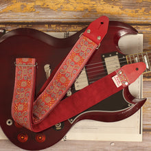 Red Andromeda guitar strap laid over an Edwards SG guitar, showing its red and orange jacquard pattern and burgundy suede backing.