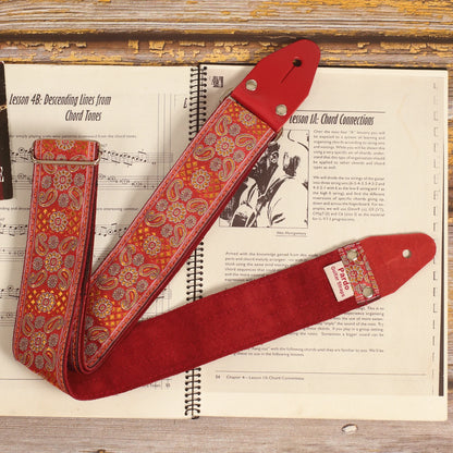 Red Andromeda guitar strap laid over a sheet music book, showing its red and orange jacquard pattern and burgundy suede backing.