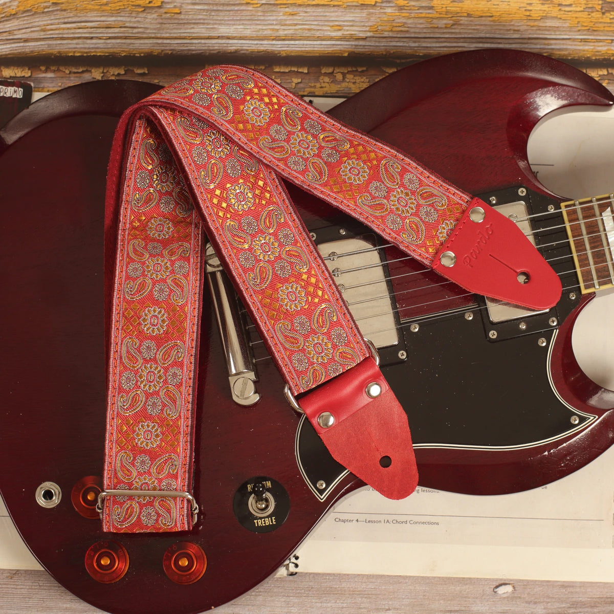 Close-up of the front of the Red Andromeda guitar strap laid over an Edwards SG guitar, showing its red and orange jacquard pattern.