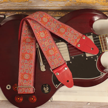 Close-up of the front of the Red Andromeda guitar strap laid over an Edwards SG guitar, showing its red and orange jacquard pattern.