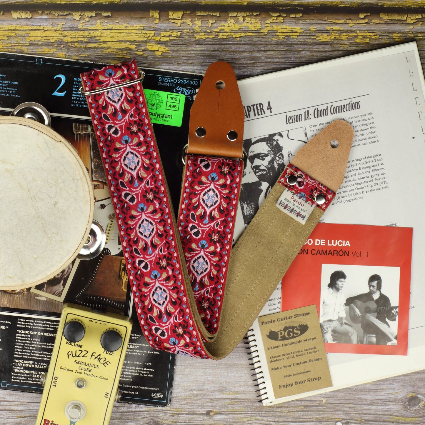 Red Pheasant guitar strap showing its jacquard pattern, Clear Brown suede backing and leather ends on a music book beside a Paco de Lucía and Camarón de la Isla CD cover