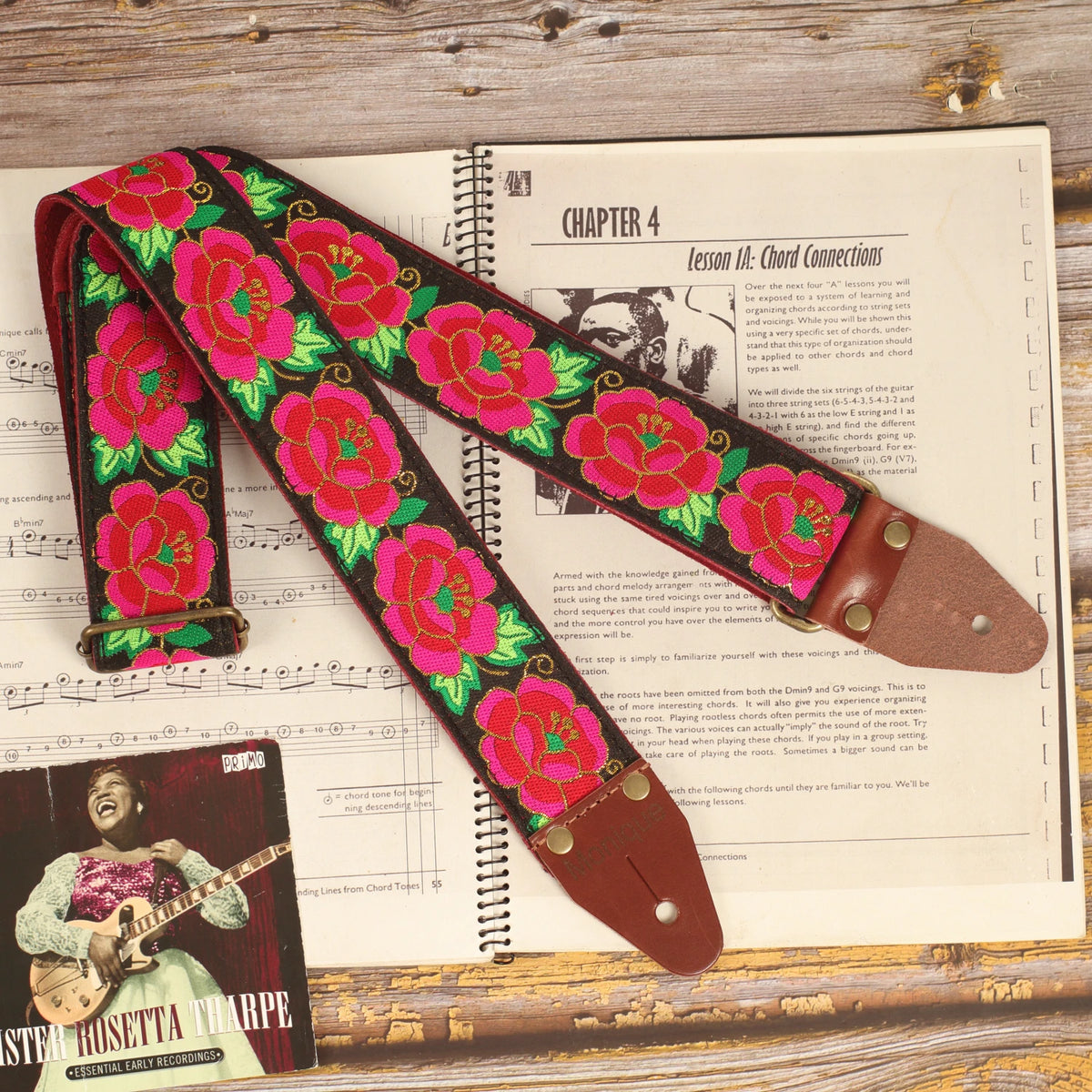 Grand Petal Red Roses jacquard guitar strap on a sheet music book with dark brown leather ends and Antique Gold hardware