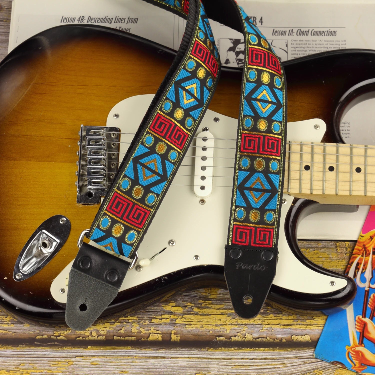 Sunstone Circuit guitar strap displayed on a sunburst Fender Stratocaster, showing its turquoise, red and golden geometric pattern.