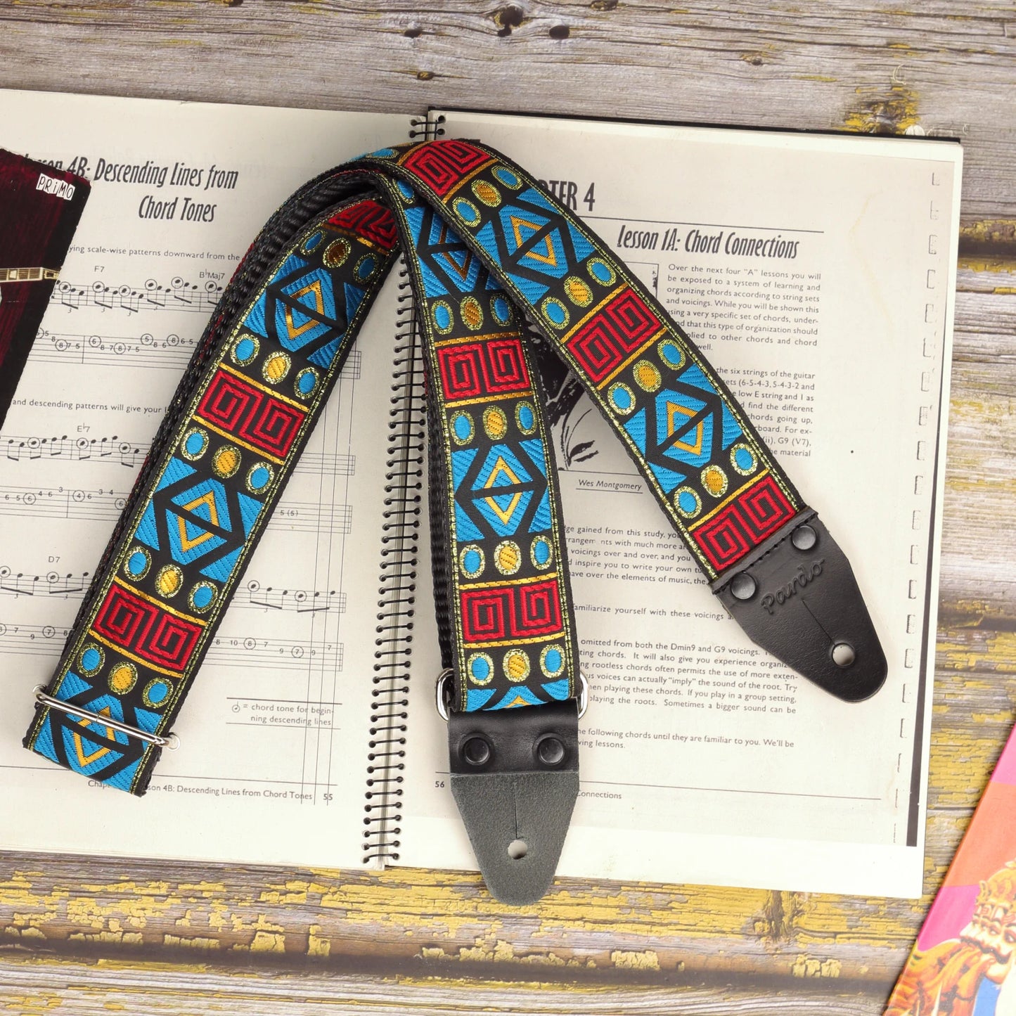 Sunstone Circuit guitar strap displayed on a sheet music book, featuring its turquoise, red and golden jacquard design.